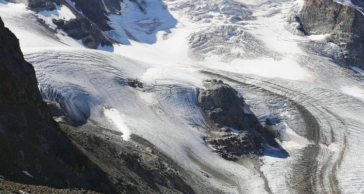 Glacier recouvert de neige avec des crevasses et des affleurements rocheux.