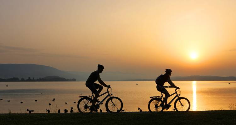 Silhouette of two cyclists during sunset by a lakeside.