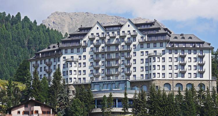 Grand bâtiment d'hôtel avec un arrière-plan montagneux sous un ciel dégagé.