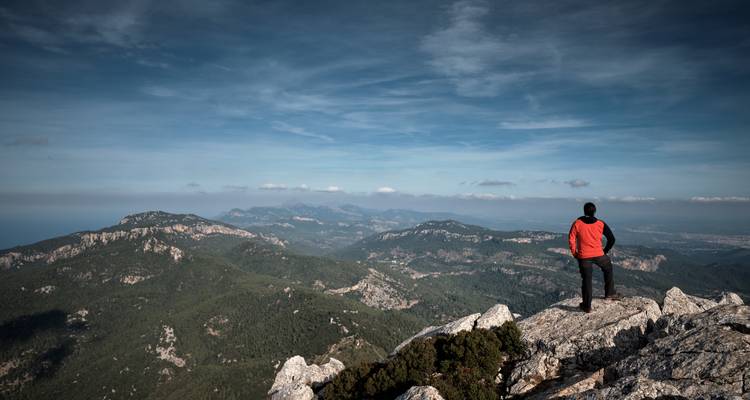 Une personne debout sur un pic rocheux surplombant un vaste paysage montagneux.