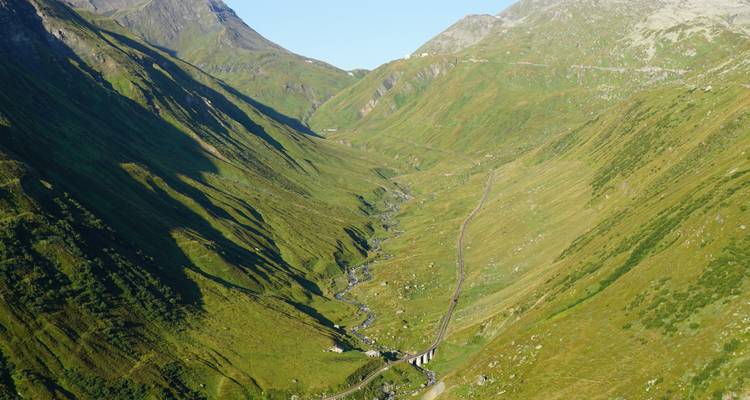 Luftaufnahme einer gewundenen Talstraße, umgeben von üppig grünen Hügeln.