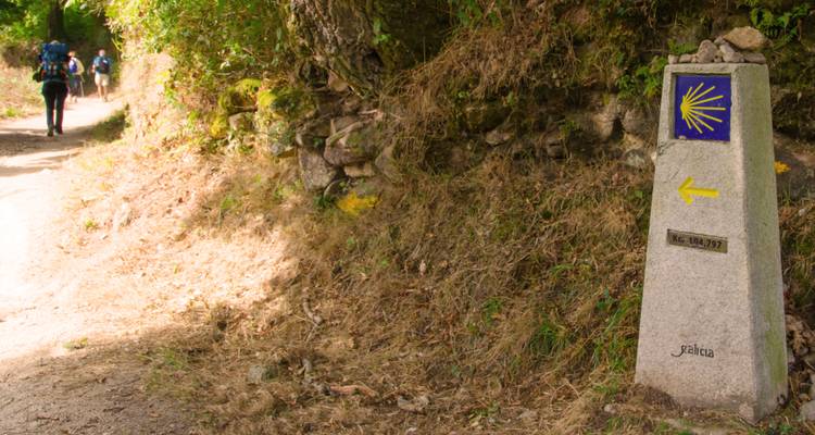 Pilger auf einem Weg mit einem Steinmarkierungszeichen mit dem Jakobsweg-Muschelsymbol.