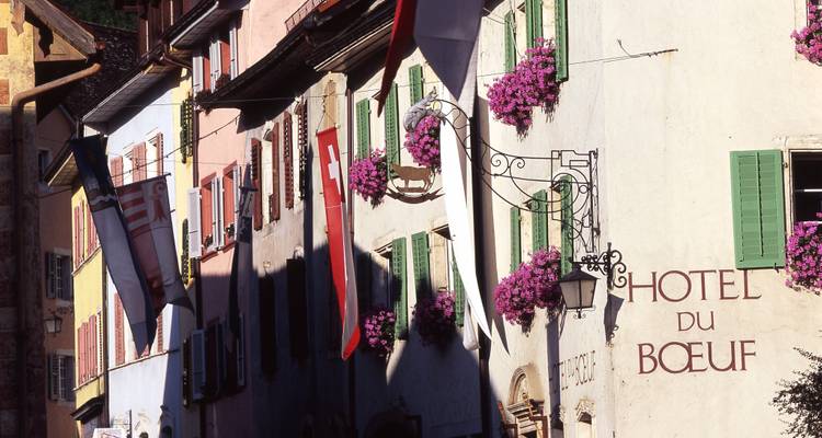 Bunte Gebäude entlang einer schmalen Straße, geschmückt mit Flaggen und Blumen.