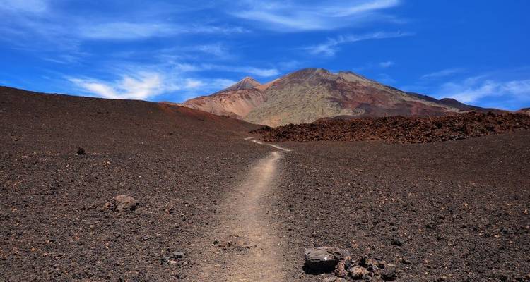 Sentier à travers un paysage volcanique accidenté avec une montagne en arrière-plan.