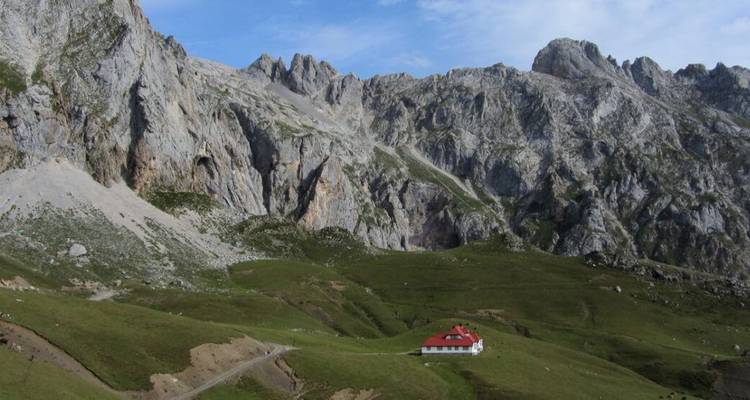 Paysage montagneux avec une petite maison dans une vallée verdoyante.