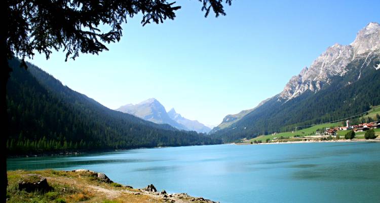 See, umgeben von Bergen mit einem kleinen Dorf am Ufer.
