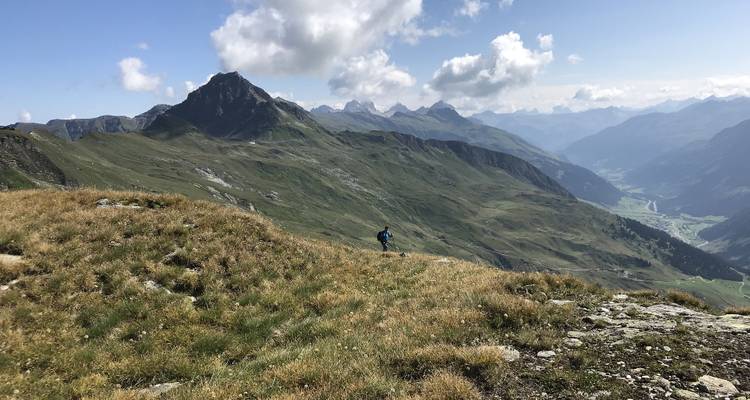Person, die entlang eines grasbewachsenen Bergrückens unter klarem Himmel wandelt