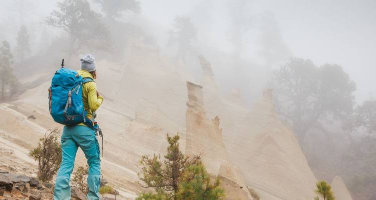Person with backpack hiking in a foggy landscape.