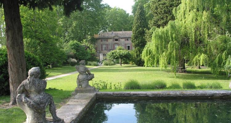 Jardin idyllique avec un étang, des statues et un bâtiment historique.