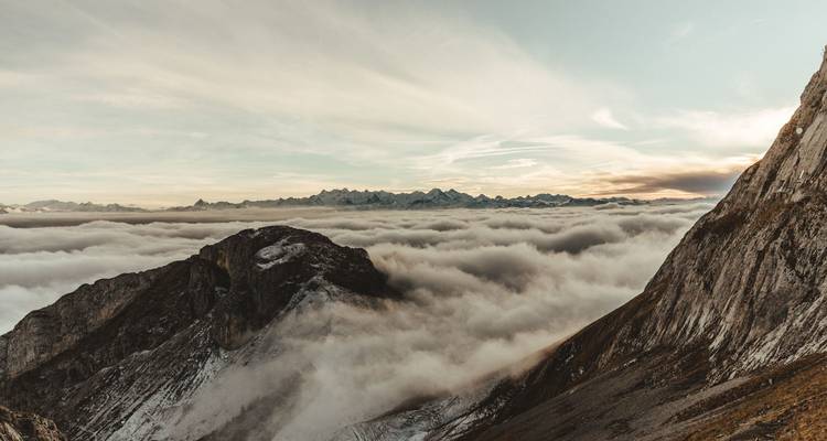 Berggipfel, die bei Sonnenuntergang aus einem Wolkenmeer hervorragen.