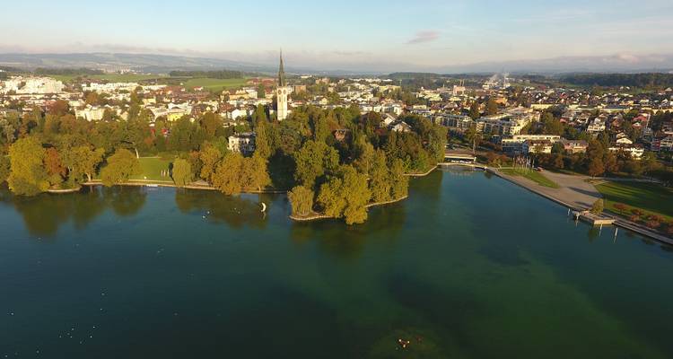 Luftaufnahme einer Stadt an einem See, umgeben von Herbstbäumen.