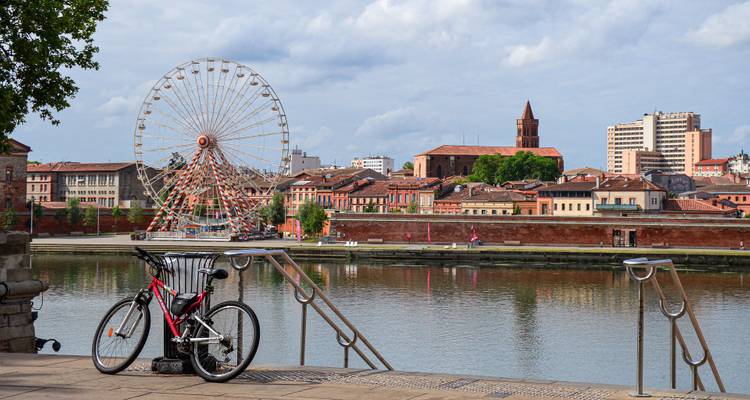 Grande roue devant un paysage urbain au bord de la rivière.