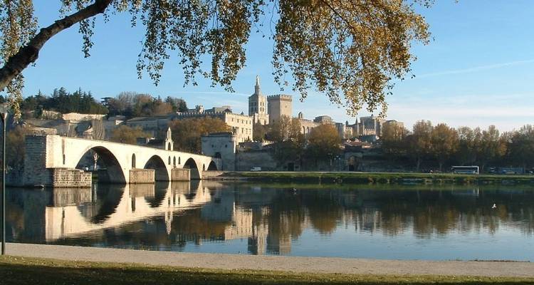 Un pont de pierre historique au-dessus d'une rivière avec des reflets et une ville en arrière-plan.