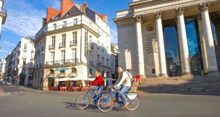 Cyclistes sur une place de ville avec des bâtiments historiques.