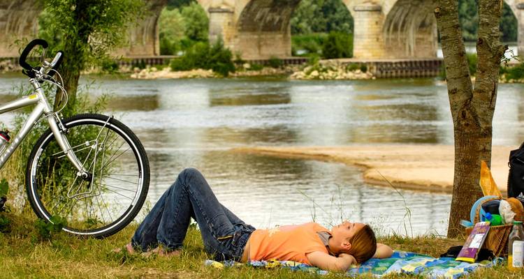 Personne se détendant au bord d'une rivière sous un arbre, avec un vélo.