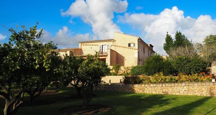 Une maison en pierre avec des jardins verdoyants sous un ciel bleu.