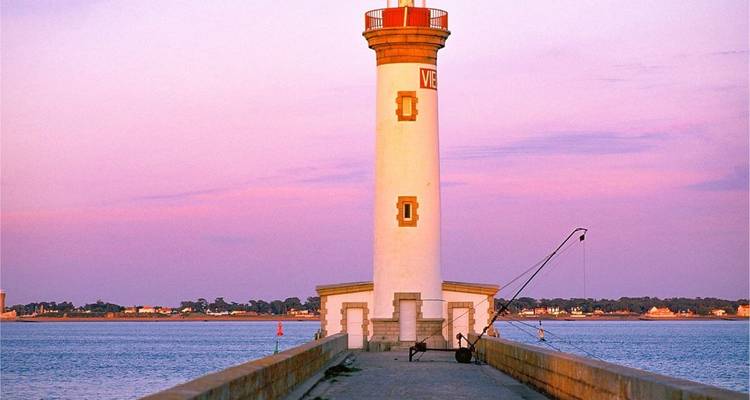 Phare sur une jetée au coucher du soleil avec un ciel rose.