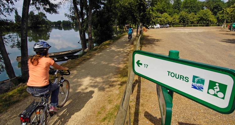 Des personnes à vélo près d'un lac avec un panneau indiquant Tours.