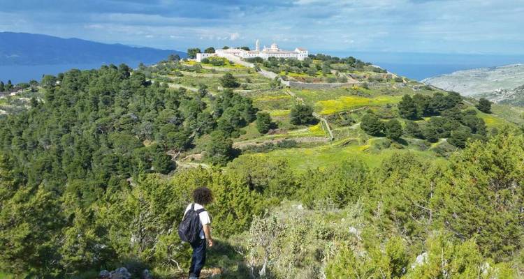 Une personne debout sur un sentier de colline avec une vue sur un monastère lointain et la verdure environnante.