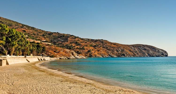 Ruhiger Sandstrand mit türkisfarbenem Flachwasser und trockenen Hügeln dahinter.
