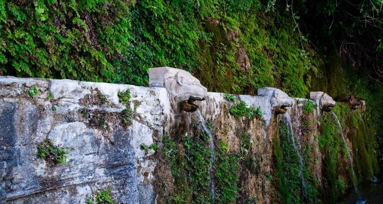 Aus Stein gemeißelte Löwenkopfbrunnen, aus denen Wasser über moosbedeckte Mauern fließt.