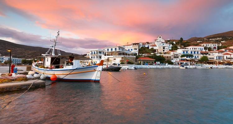Fischerboot, das bei Sonnenuntergang in einem Hafen mit Pastellhimmeln über einem griechischen Dorf vertäut ist.
