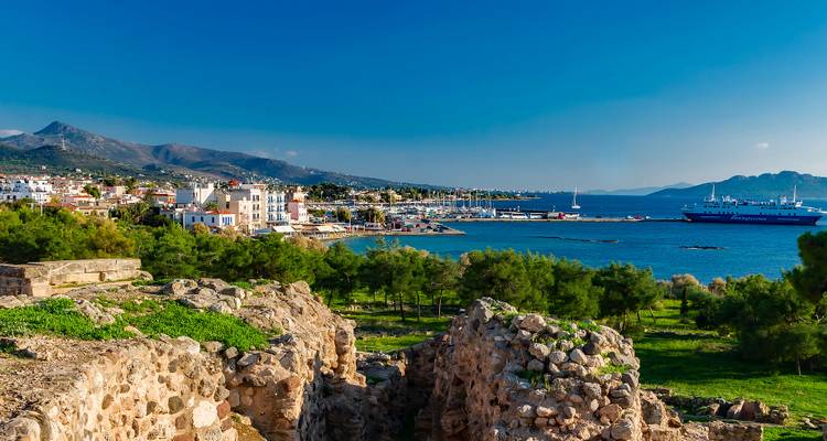 Ville côtière avec bateaux et ruines au premier plan.