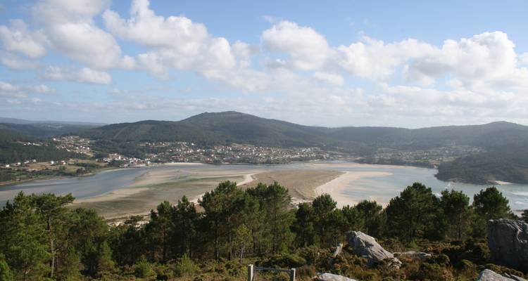 Ein Panoramablick auf ein Küstengebiet mit einem Sandstrand, Hügeln und einer Stadt in der Ferne.