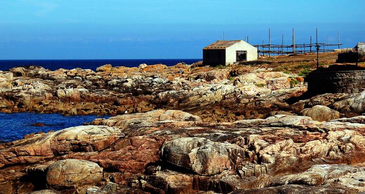 Ein Küstenblick mit einer zerklüfteten, felsigen Küstenlinie und kleinen Bauwerken nahe dem Meer.