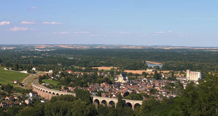 Une vue de paysage avec un viaduc, une ville, et une rivière qui coule à travers une vallée luxuriante.