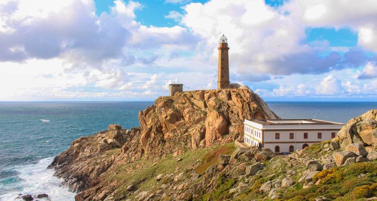 Un phare perché sur une falaise rocheuse surplombant la mer sous un ciel partiellement nuageux.