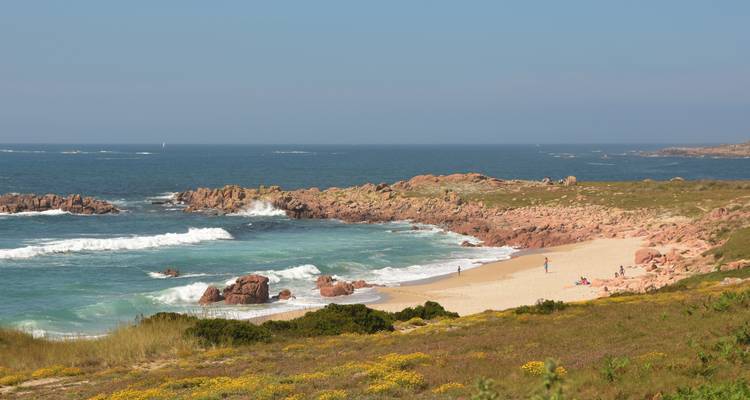 Une plage isolée avec des affleurements rocheux et des vagues douces par une journée ensoleillée.