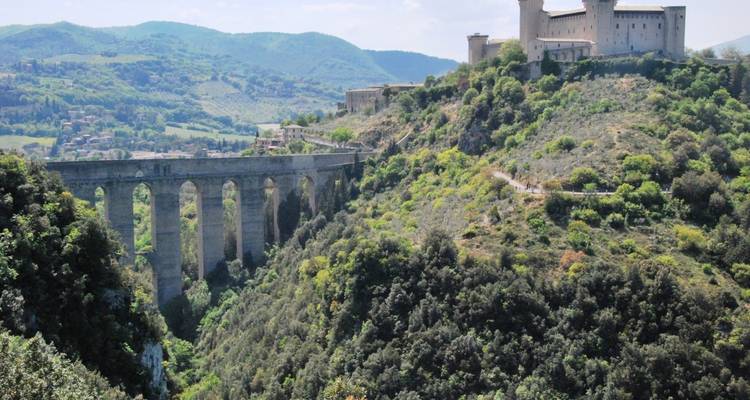 Ancien aqueduc en pierre et forteresse sur une colline verdoyante.
