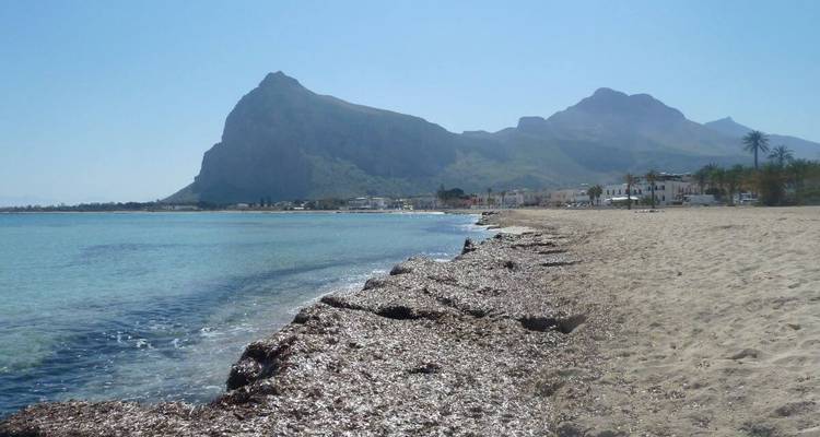 Plage de sable avec un arrière-plan montagneux et une mer sereine.