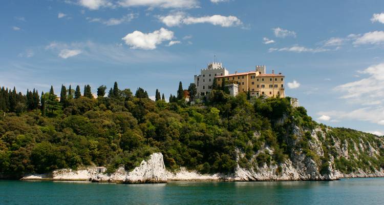 Klippenschloss mit charakteristischer Architektur und Zypressen darunter.