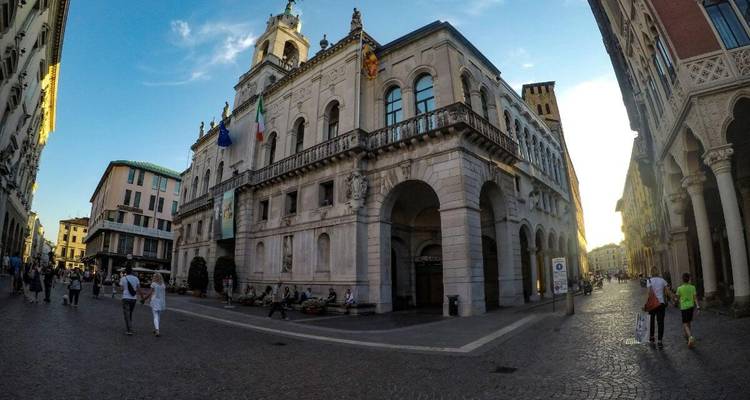 Historisch gebouw op een stadsplein met wandelende mensen.