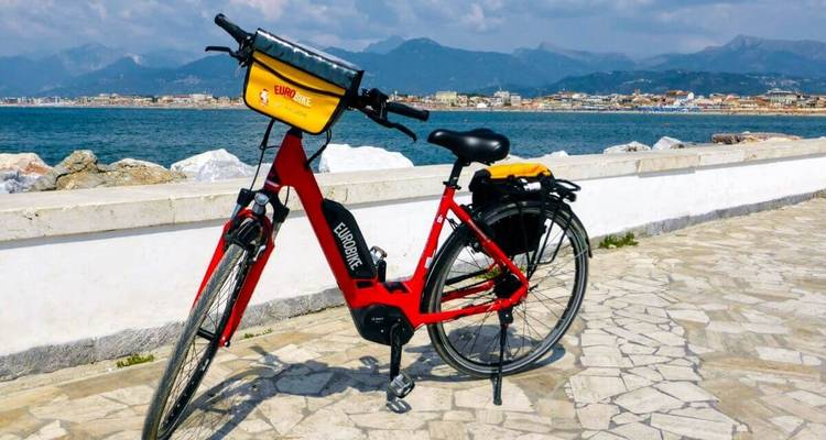 Ein Fahrrad, das auf einer Promenade mit Meer- und Bergblick geparkt ist.