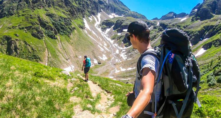 Two hikers on a mountain trail, one looking back at the camera.