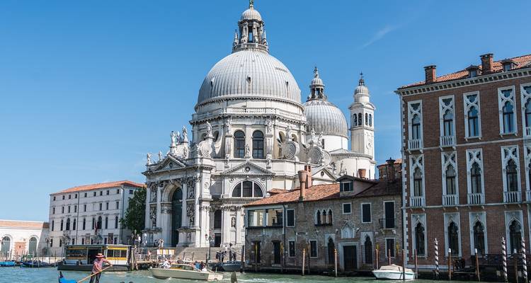 Gran iglesia barroca junto a un canal con barcos y cielo azul.