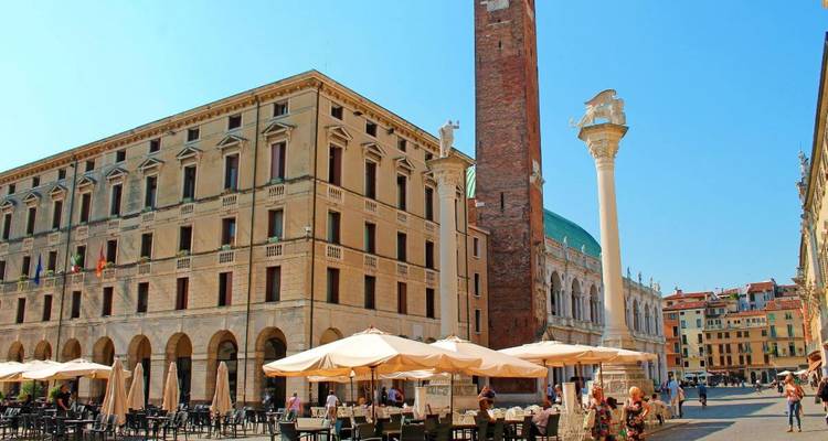 Plaza histórica con una torre del reloj y cafés.