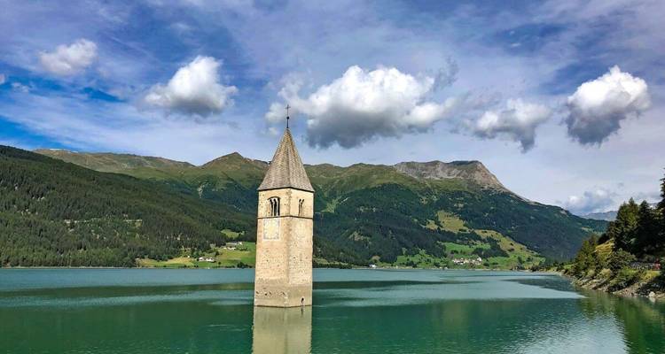 Submerged bell tower in a lake with mountains.