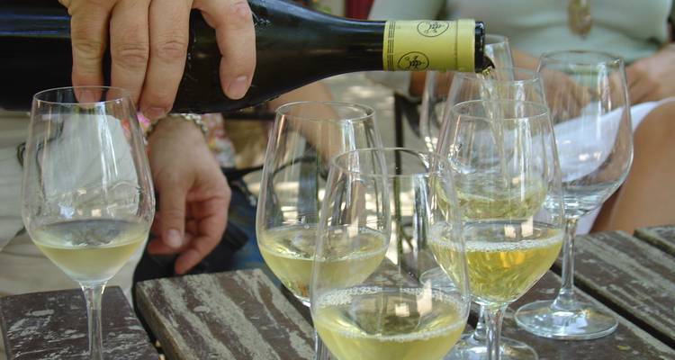 Gros plan d'une main versant du vin blanc dans des verres.