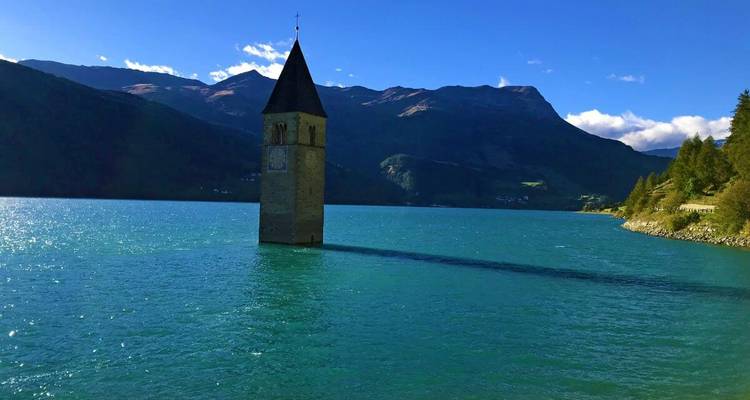 El famoso campanario sumergido se alza aislado en el lago turquesa de Reschen con picos alpinos al fondo.