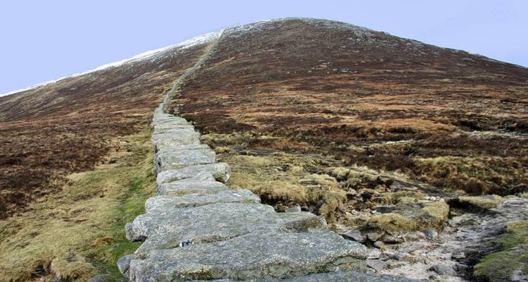 Escalera de piedra empinada de la Muralla de Mourne ascendiendo por una ladera de montaña árida.