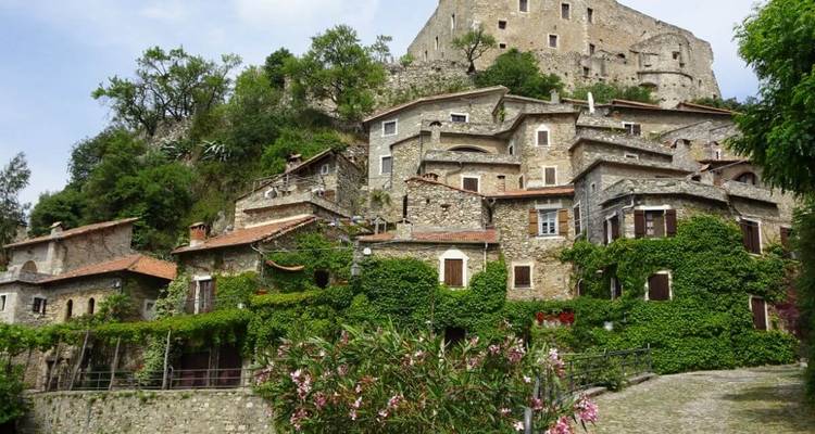 Alte Steinhäuser mit Grün bewachsen an einem Hang.