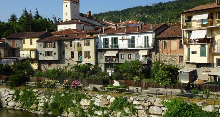 Bunte Häuser entlang eines Flussufers mit einem Turm im Hintergrund.