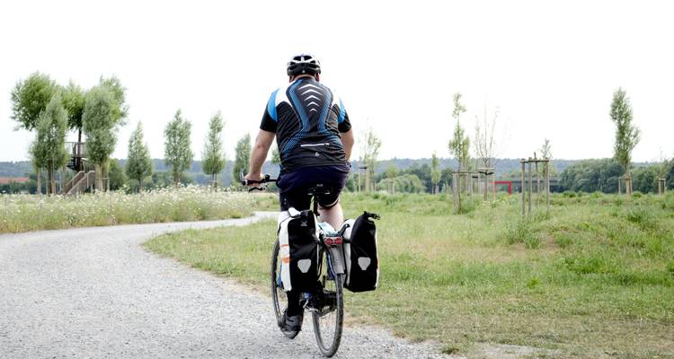 Personne faisant du vélo sur un sentier de gravier à travers un paysage rural.