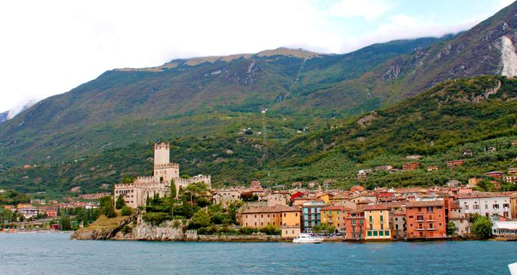 Kasteel en gebouwen langs een meeroever met bergen.