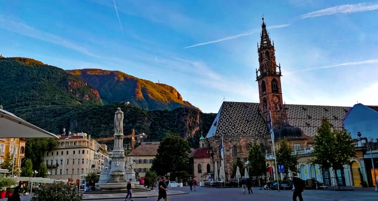 Standbeeld en kerk met een bergachtergrond tijdens zonsondergang.