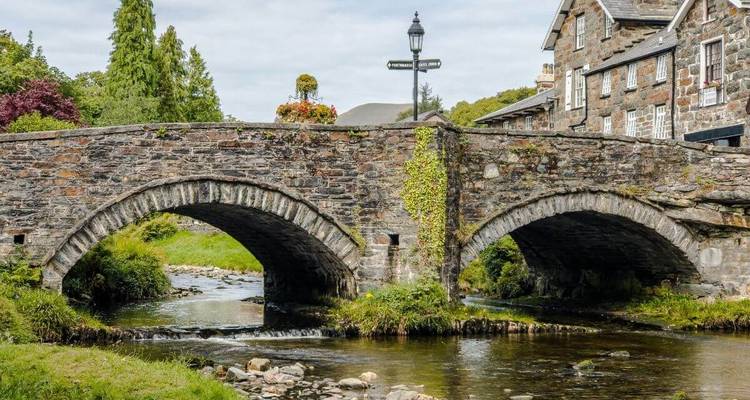 Historische, doppelt gewölbte Steinbrücke über einen klaren Bach neben Dorfhäuschen